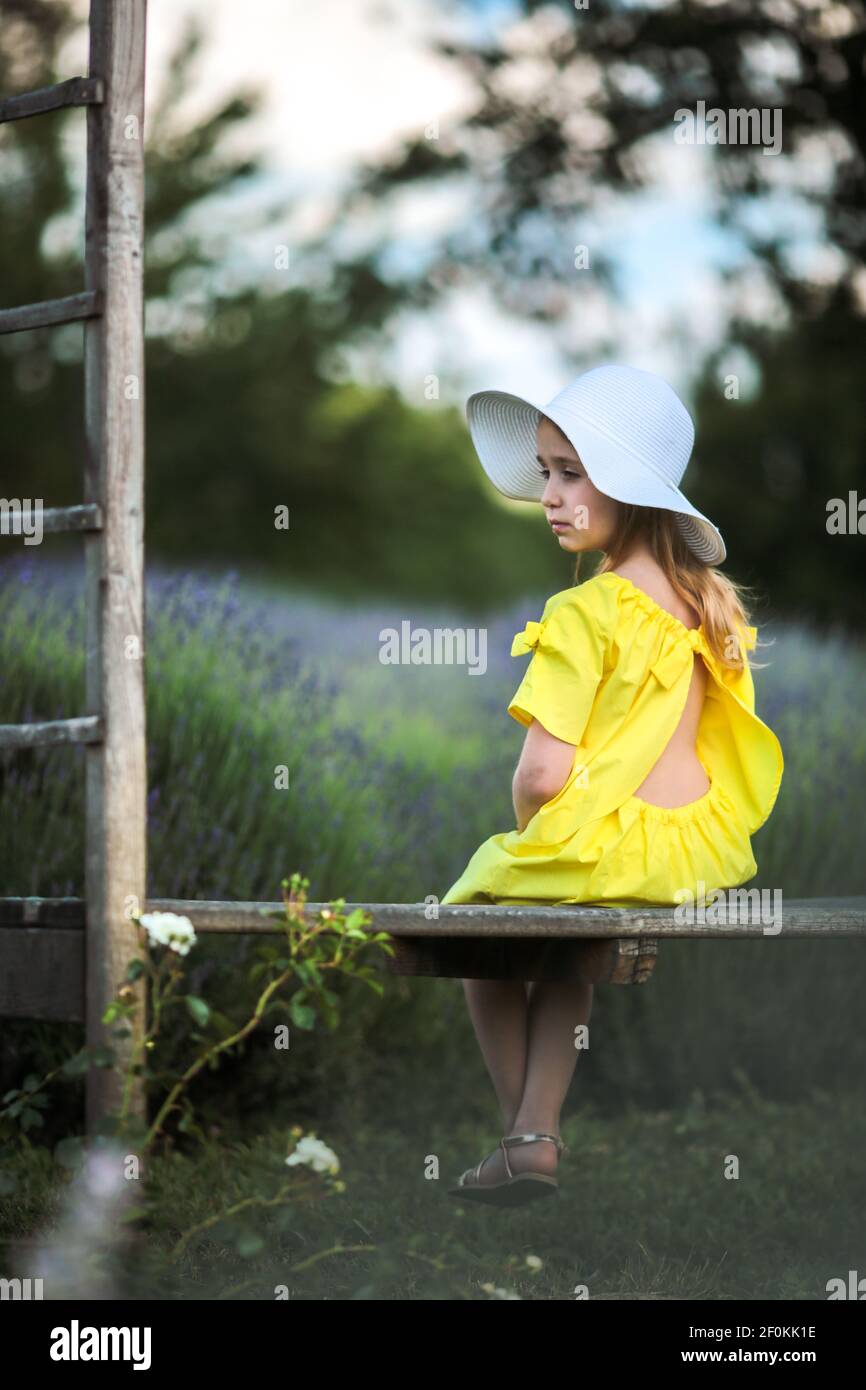 Beautiful little girl in a yellow dress and white hat sitting on a ...