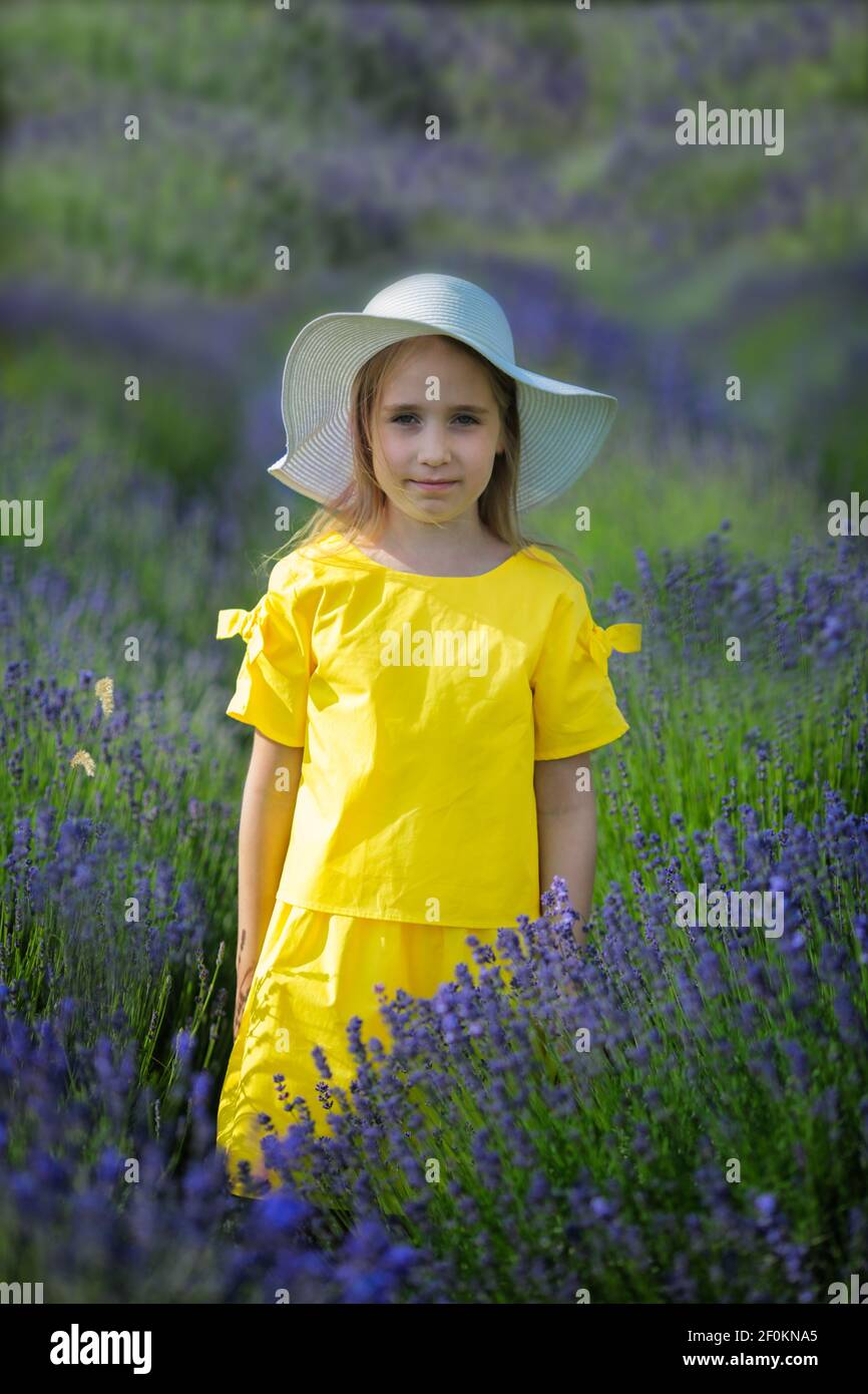Beautiful little girl in a yellow dress and white hat walking in a ...