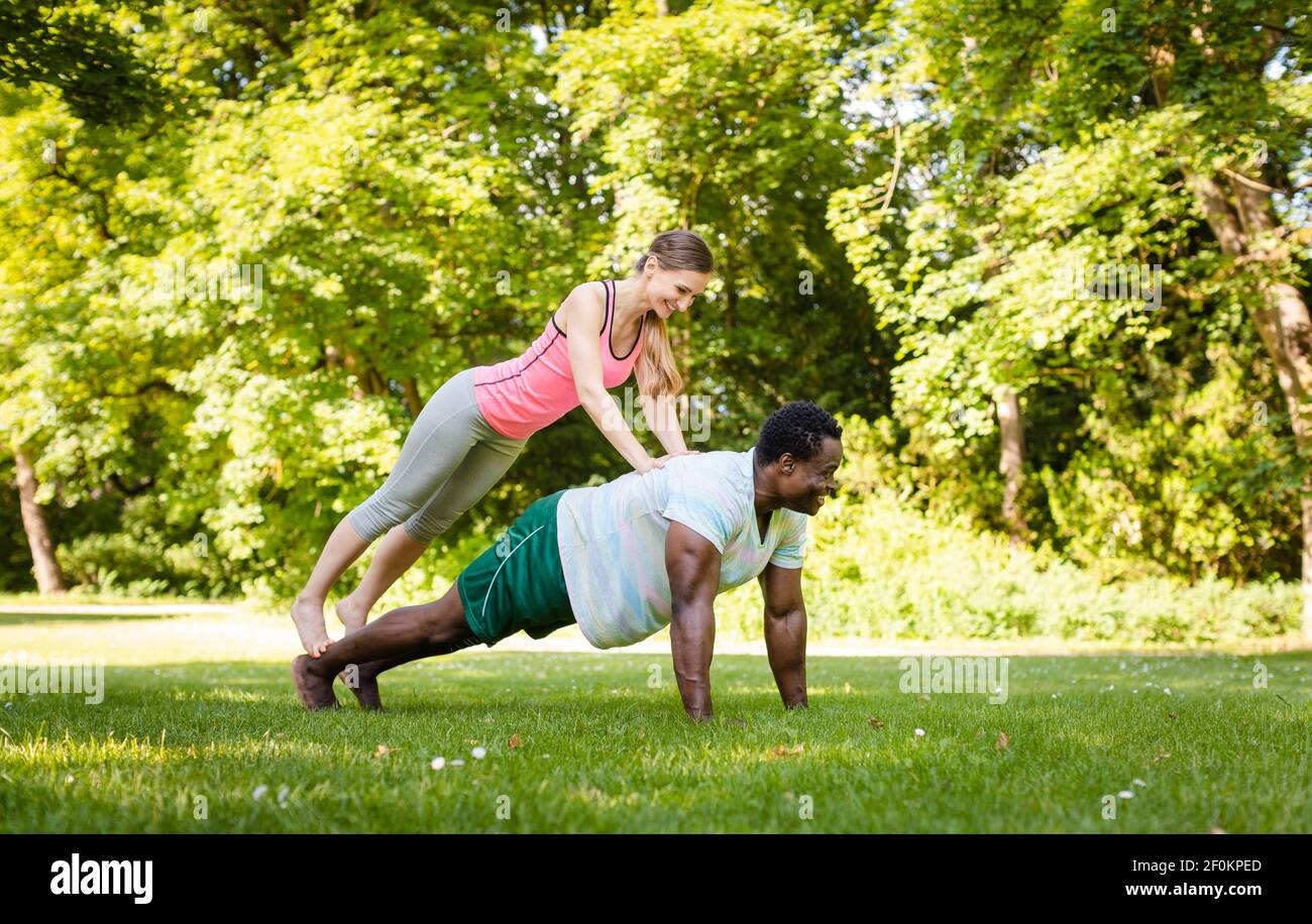 Mixed race couple doing fitness pushups in the park Stock Photo