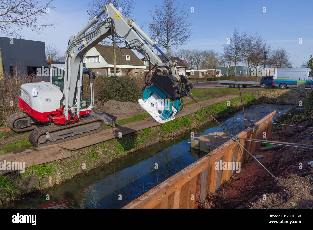 Construction workers are placing anchors for a wooden retaining wall for a garden along a canal Stock Photo