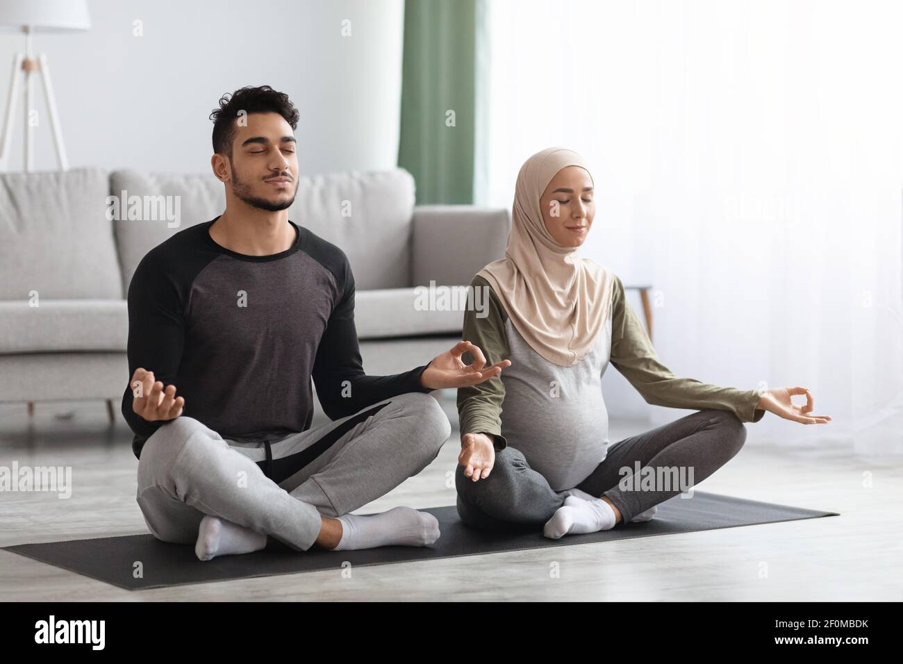 Pregnant muslim couple practicing prenatal yoga at home, meditating together Stock Photo