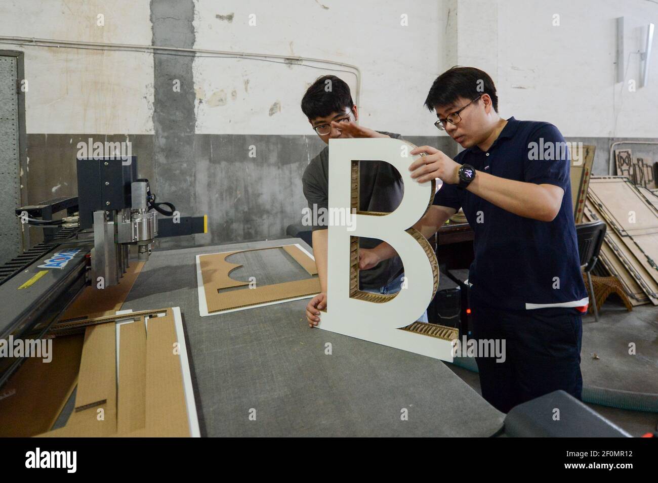 In this undated photo, Chinese man Zheng Majun, right, and his team assemble an alphabet made of discarded cardboard boxes at the workshop in Haiyan county, Jiaxing city, east China's Zhejiang province. Chinese man Zheng Majun started his business in packaging after graduated in Haiyan county, Jiaxing city, east China's Zhejiang province. He found that many parents were required to help their kids create artworks made of discarded cardboard boxes. After doing market research and development for more than a year, Zheng started a business in toys made of paper. His design team first created thre Stock Photo