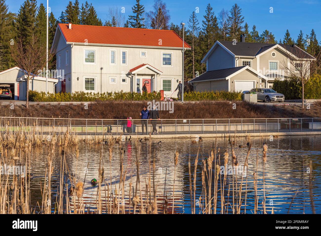 Beautiful spring landscape view. Family with child walking near local pond. Another family leaving their home for walking. Uppsala.  Sweden Stock Photo