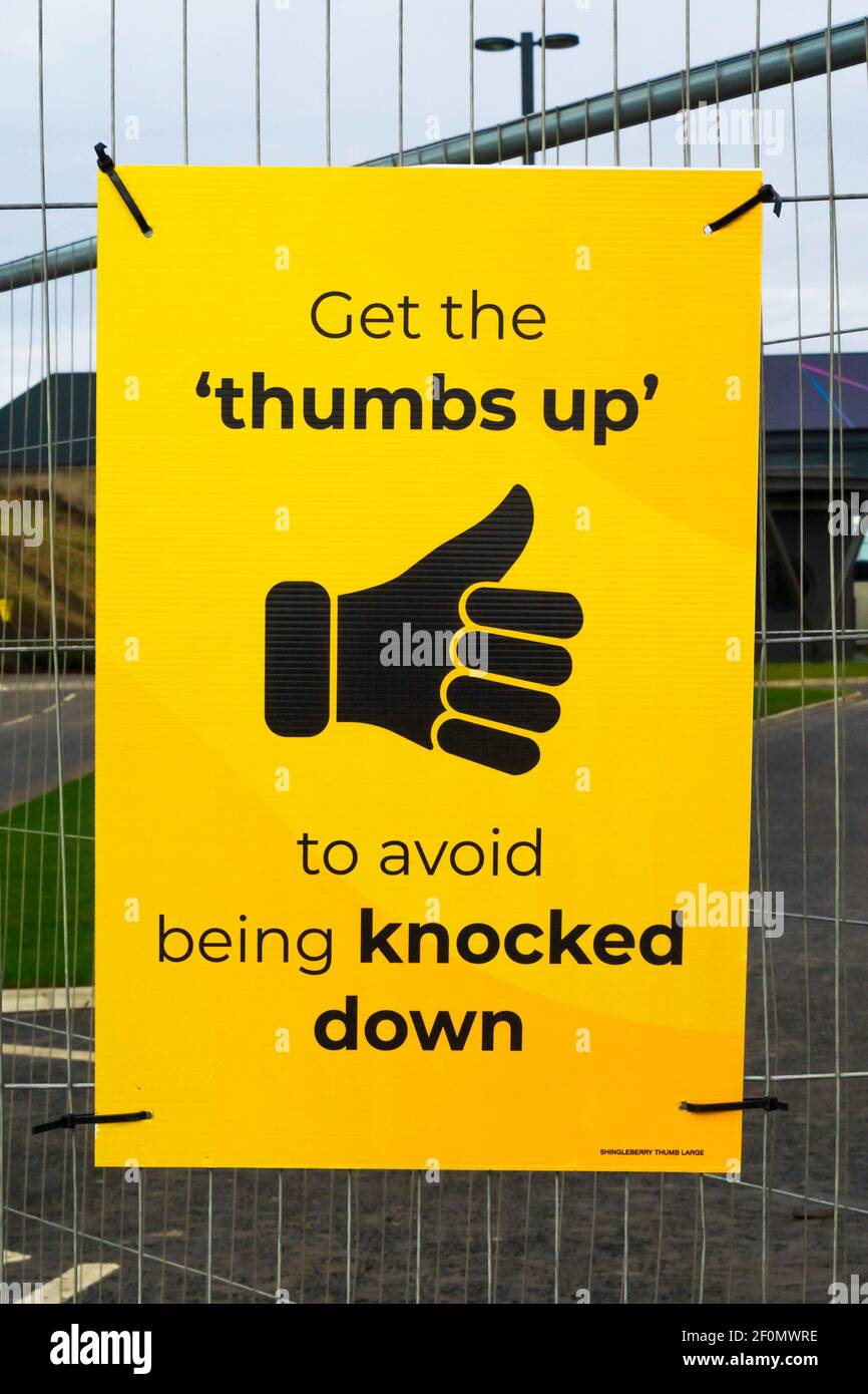 A yellow and black sign saying 'Get the thumbs up, to avoid being knocked down' advising to look for the sign when a road is safe to cross Stock Photo