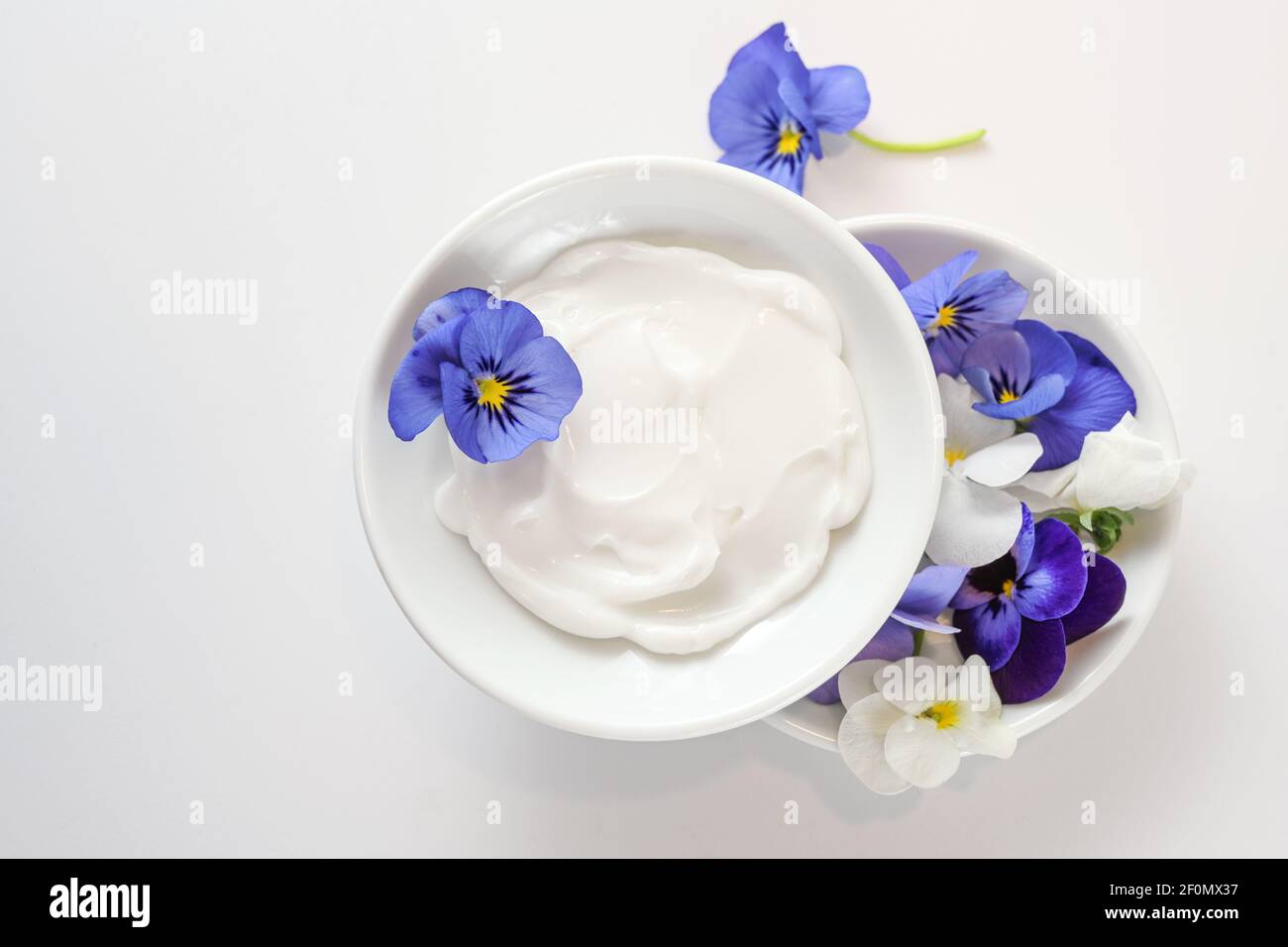 Natural cosmetic ointment and viola or violet flowers in white bowls on a light gray background, copy space, high angle view from above, selected focu Stock Photo