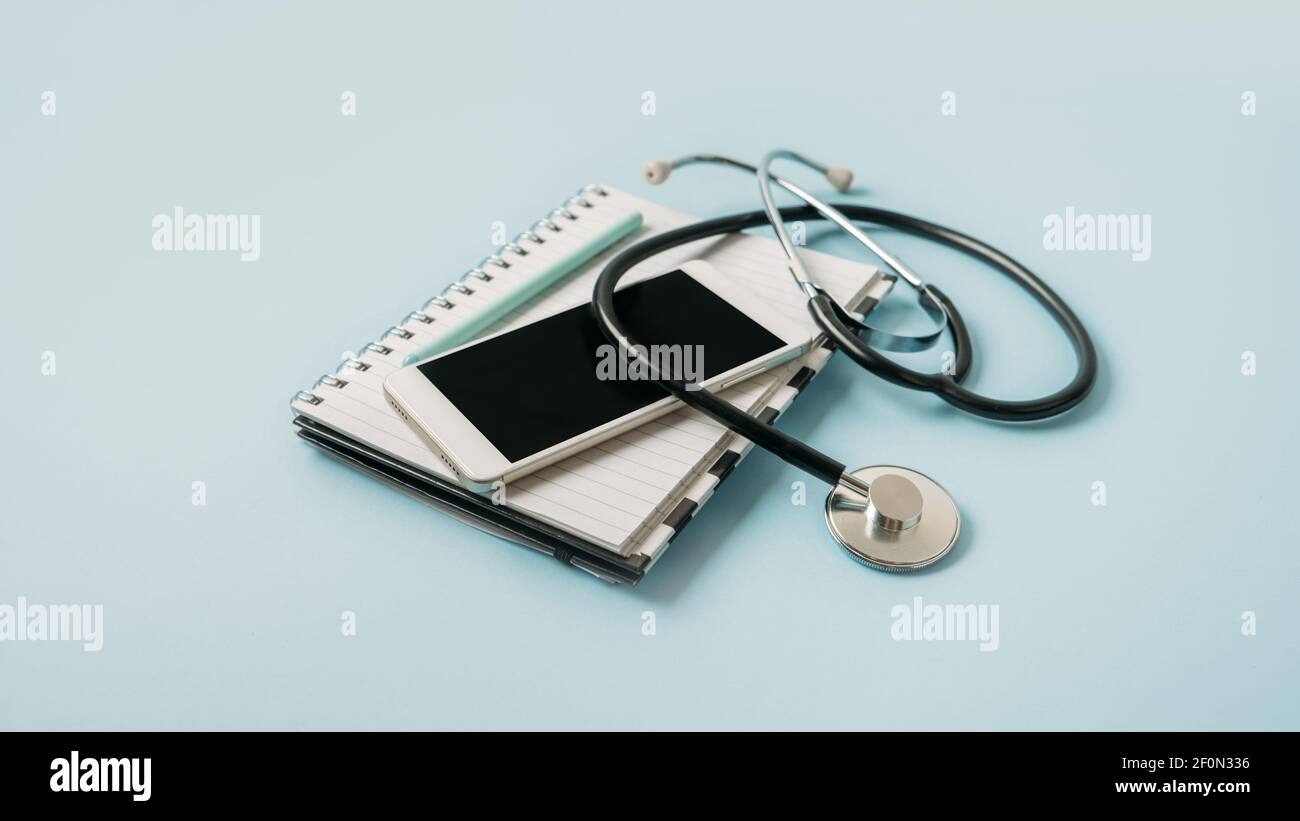 Telemedicine or telehealth virtual visit, video visit, remote doctor video chat consultation concept with smartphone, open notepad and stethoscope on Stock Photo