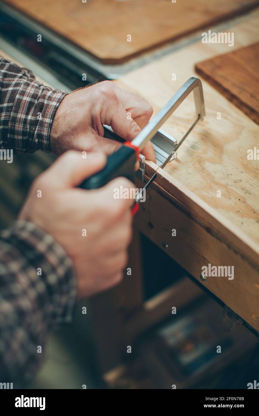 A Caucasian, middle aged man works on a small piece of a wooden airplane in his garage. Stock Photo