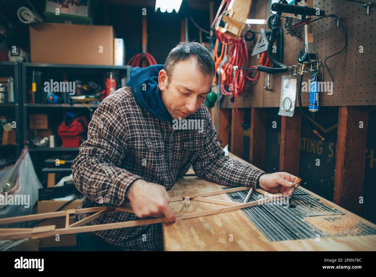A Caucasian, middle aged man works on a small piece of a wooden airplane in his garage. Stock Photo