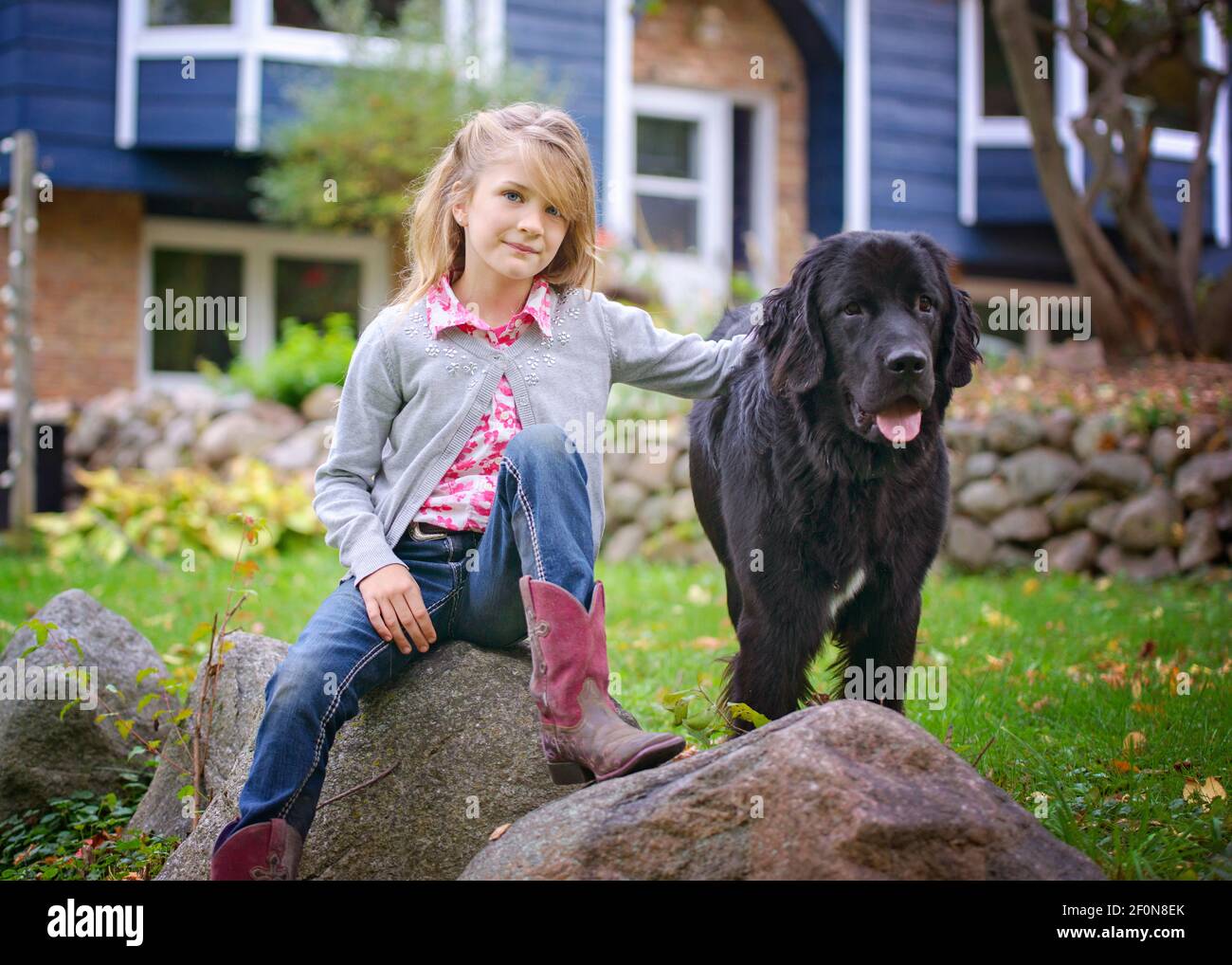 Young Blond Girl Sitting outside on a Rock with Big Black Dog Stock ...