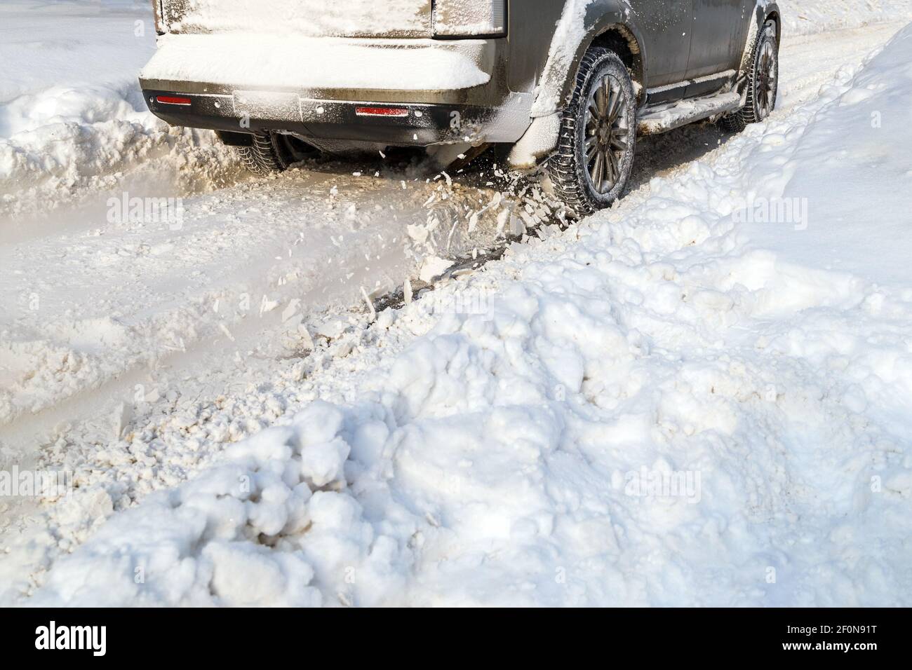Road snow flies up from a vehicle's spinning wheel. Car's wheels spin and spew up pieces of snow