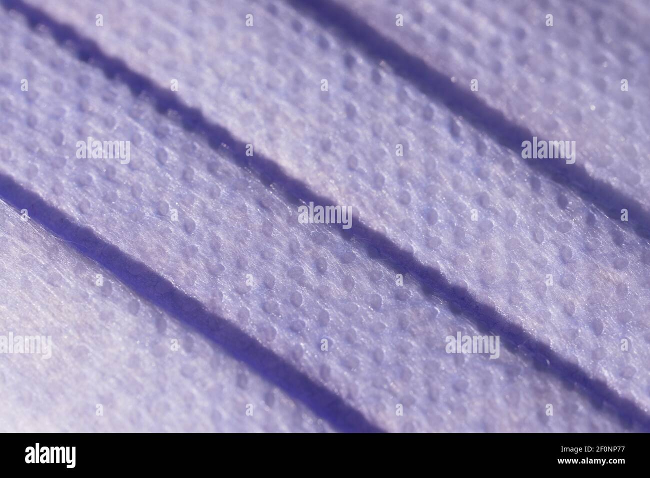 Super macro image showing the surface texture of a 3 ply single use face mask. Medical mask with 3 folds, splash proof and filtering ability. Stock Photo