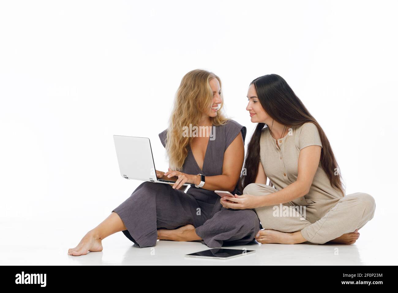 Young attractive women sit on floor, working on laptop, tablet computer and smarthphone. Two blogger girls write the text to internet blog. Stock Photo