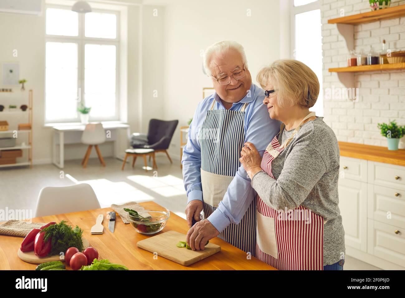 Happy senior husband and wife helping each other while cooking healthy lunch at home Stock Photo