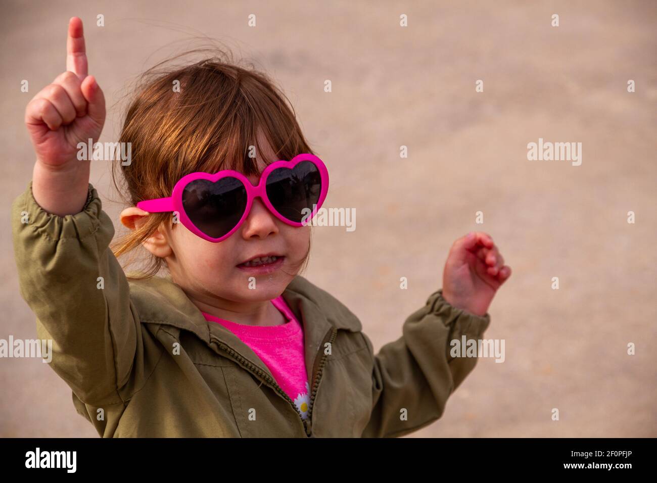 A cute, brown-haired baby girl wearing pink sunglasses and a green jacket Stock Photo