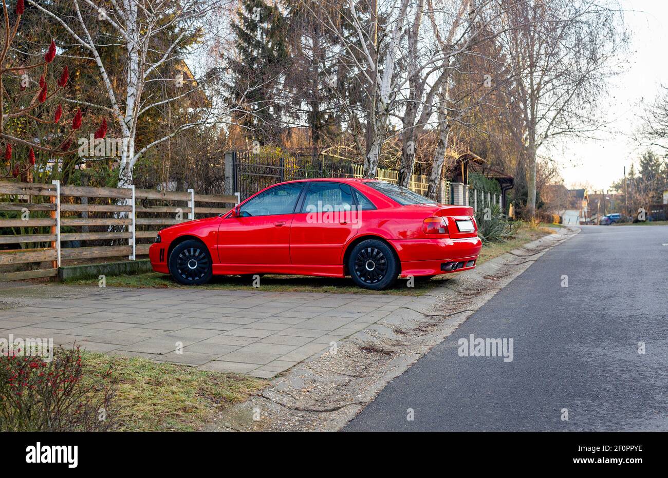Beautiful red car parked on rural street near the fence Stock Photo