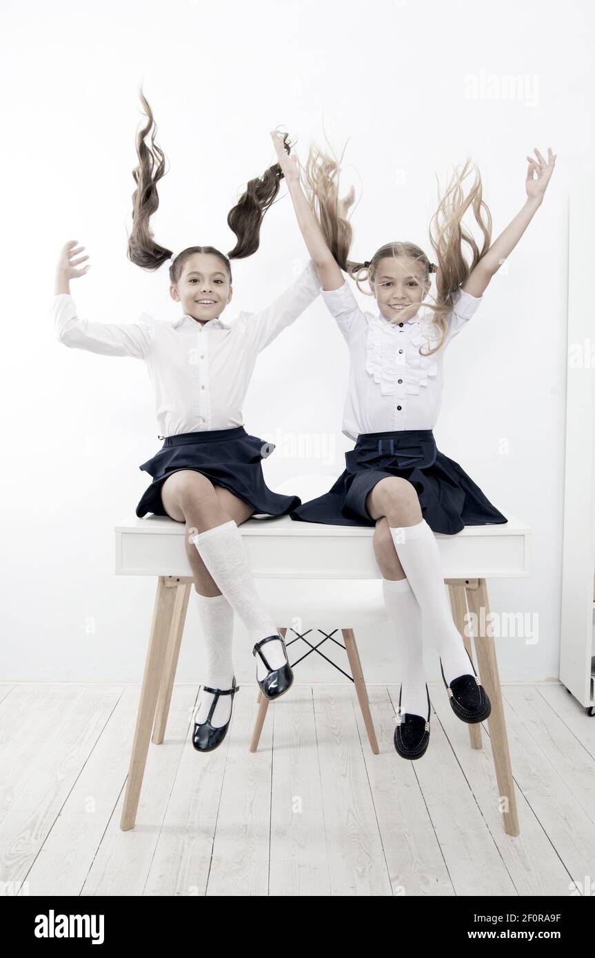 School break concept. Schoolgirls cute pony tails hairstyle sit on desk. Best friends free having fun play with hair. Perfect schoolgirls with tidy fancy hair. School hairstyles ponytails in mid air. Stock Photo