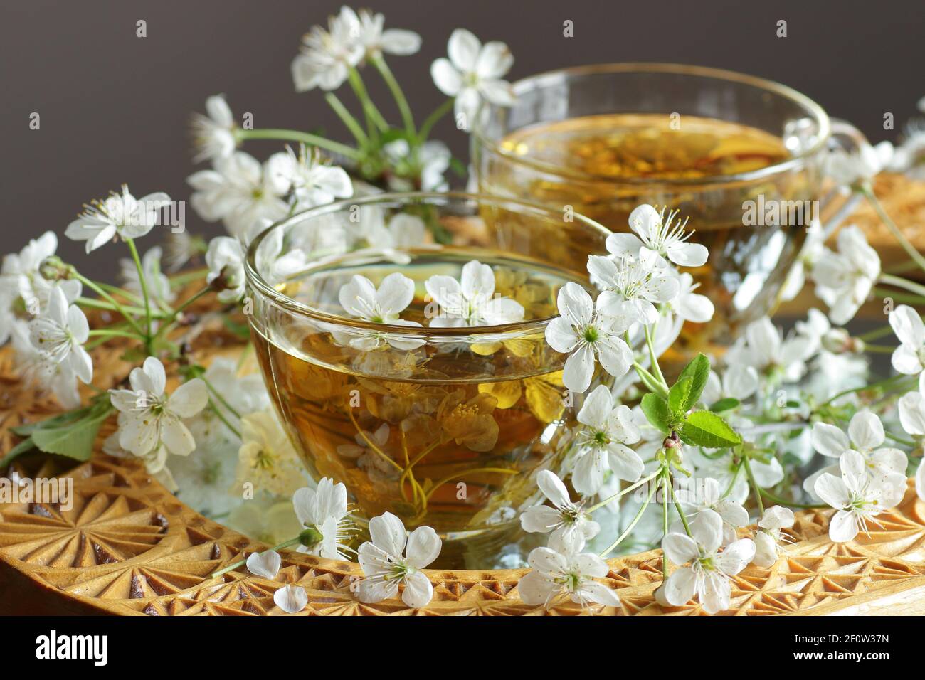Cherry blossom tea in a glass cup with blooming floral branches nearby, healthy herbal drink is
