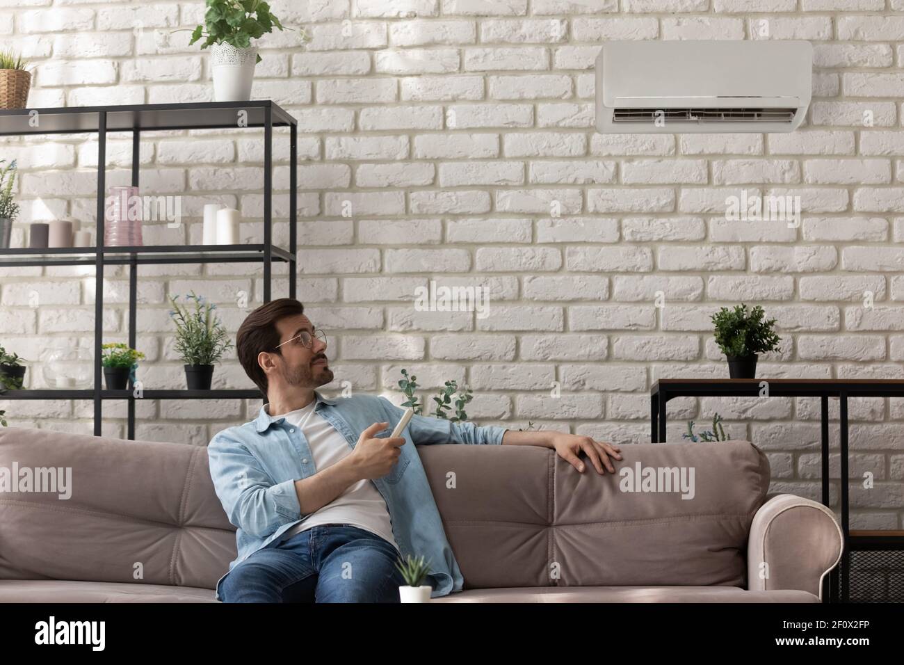 Happy young man sit on couch hold air conditioner controller Stock Photo