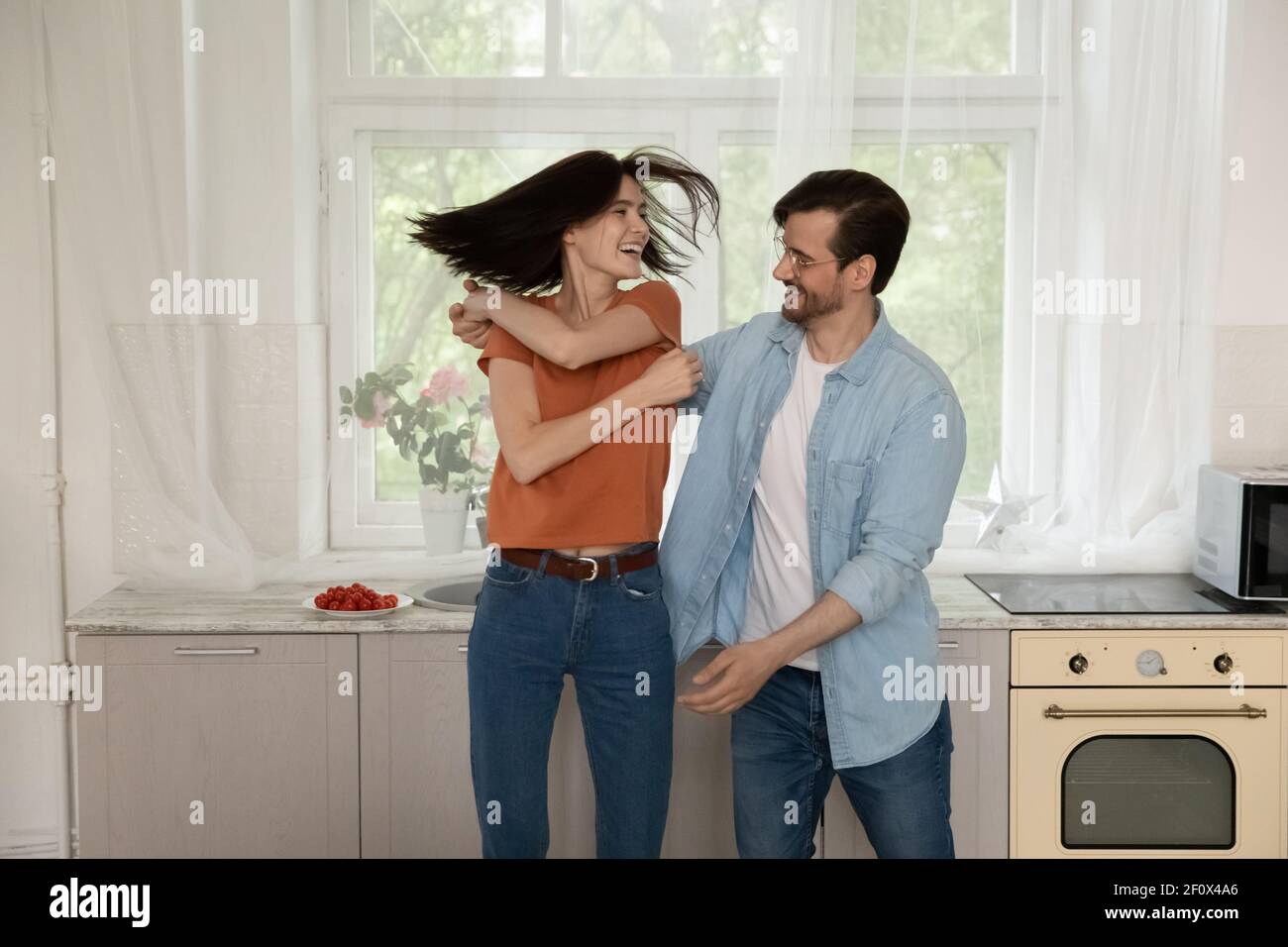 Happy young husband spin wife in funny dance at kitchen Stock Photo