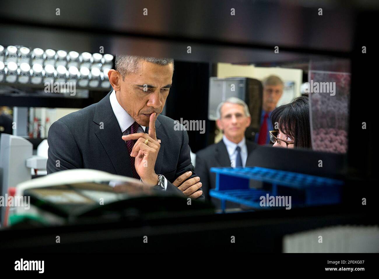 President Barack Obama listens to Dr. Nancy Sullivan during a lab tour at the Vaccine Research Center at the National Institutes of Health in Bethesda, Md., Dec. 2, 2014. Dr. Anthony Fauci, Director, National Institute of Allergy and Infectious Diseases and Dr. Francis Collins, Director, NIH watch in the background. Stock Photo