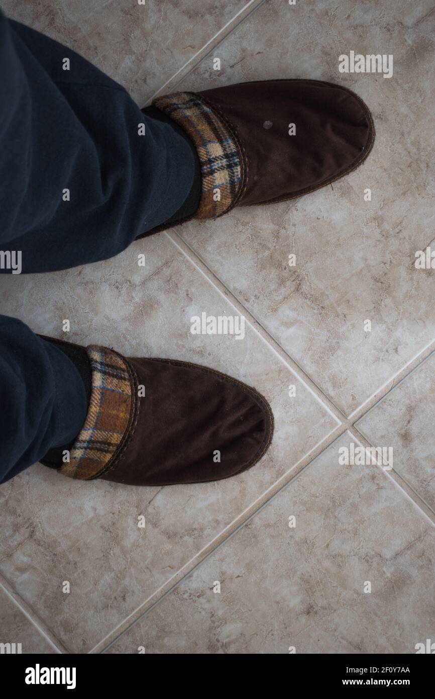 A pair of winter comfortable slippers over tiles floor. Man in warm slippers at home.Bed shoes accessory footwear.Top view Stock Photo