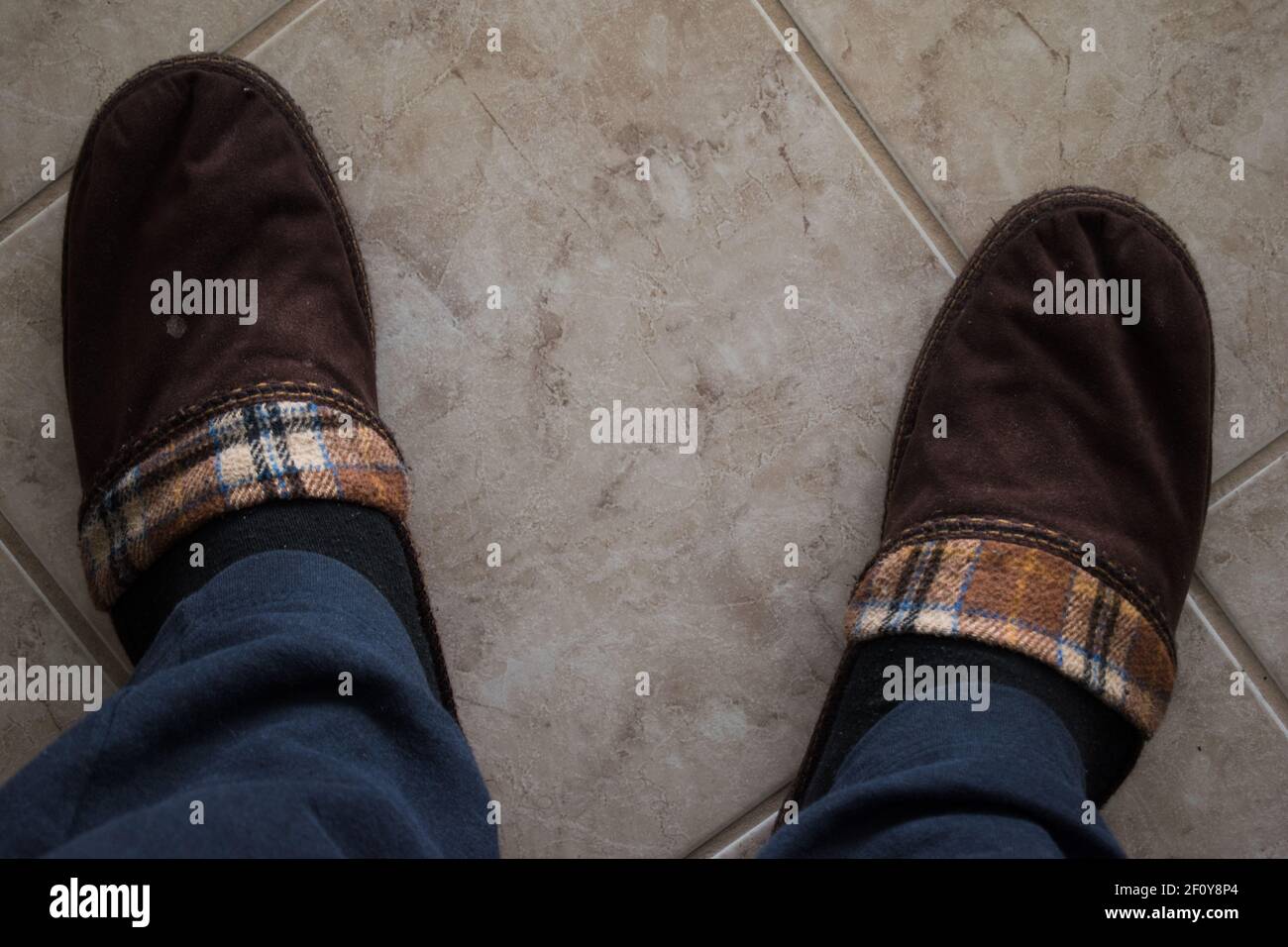A pair of winter comfortable slippers over tiles floor. Man in warm slippers at home.Bed shoes accessory footwear.Top view Stock Photo
