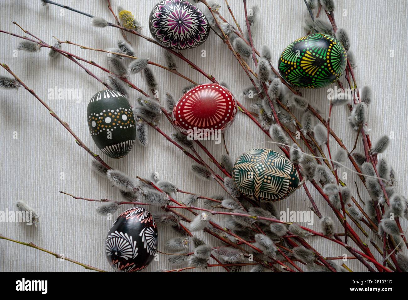 Easter flat lay with a group of Easter eggs between willow twigs with buds on a beige background. Close up. Multicolored eggs painted Stock Photo