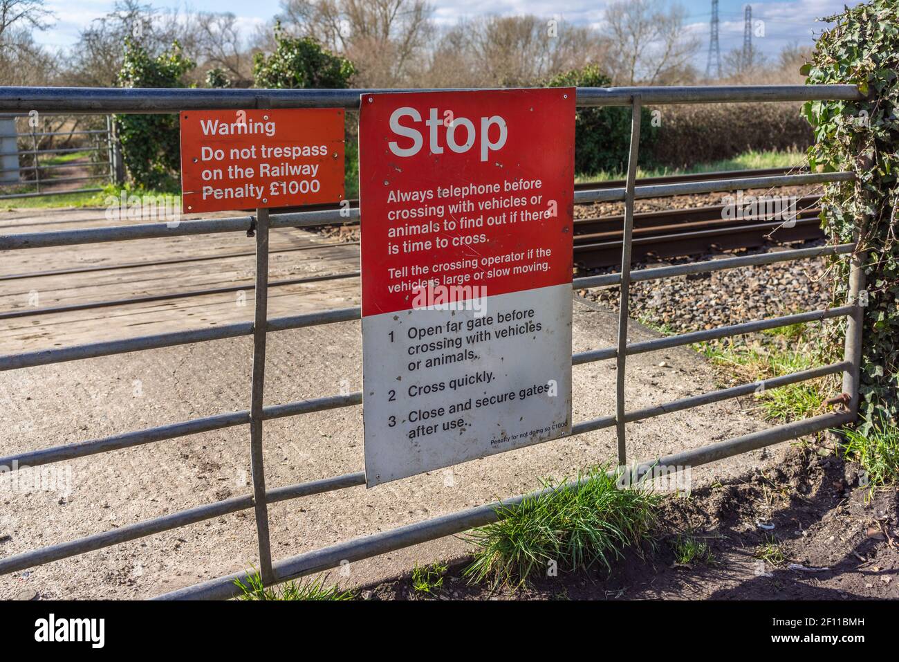 Red Stop attention do not trespass warning sign on a gate at a level railway crossing in England, UK Stock Photo