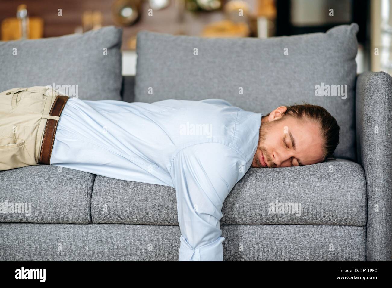 Tired guy, businessman or student dressed in formal clothes, lying on the couch, tired of work or study, collapsed from fatigue, at home in the living room, need a rest or vacation Stock Photo