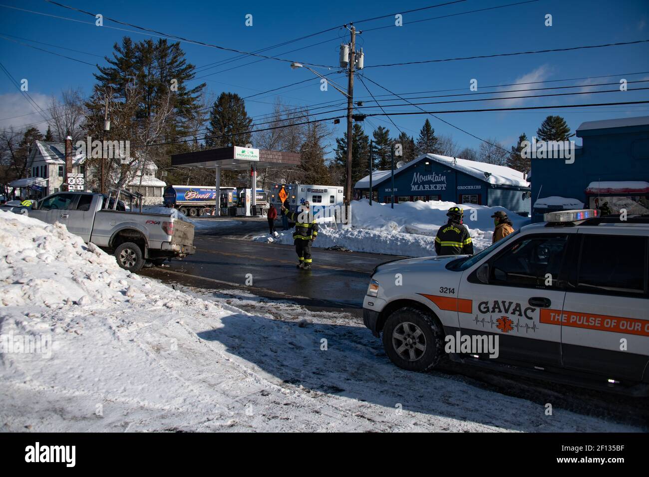 Vehicle accident scene with firemen directing traffic an ambulance and EMT on standby and a truck stuck in the snow bank. Stock Photo