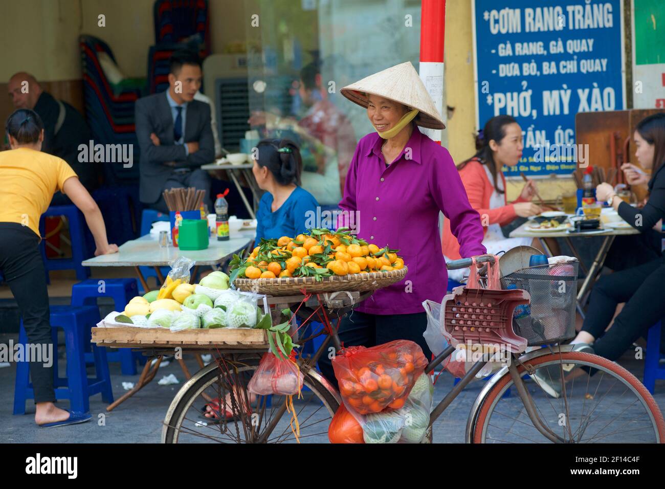 Vietnamese street life. Itinerant fruit vendor with bicycle besides roadside cafe. Hanoi, Vietnam Stock Photo