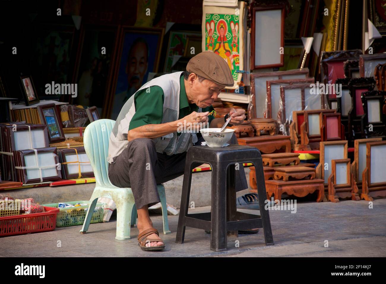 Vietnamese man eating a bowl of pho on a chair / stool outside his at