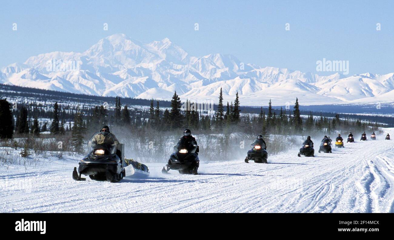 A line of snow machines cruise along the Denali Highway with Mount McKinley and the Alaska Range