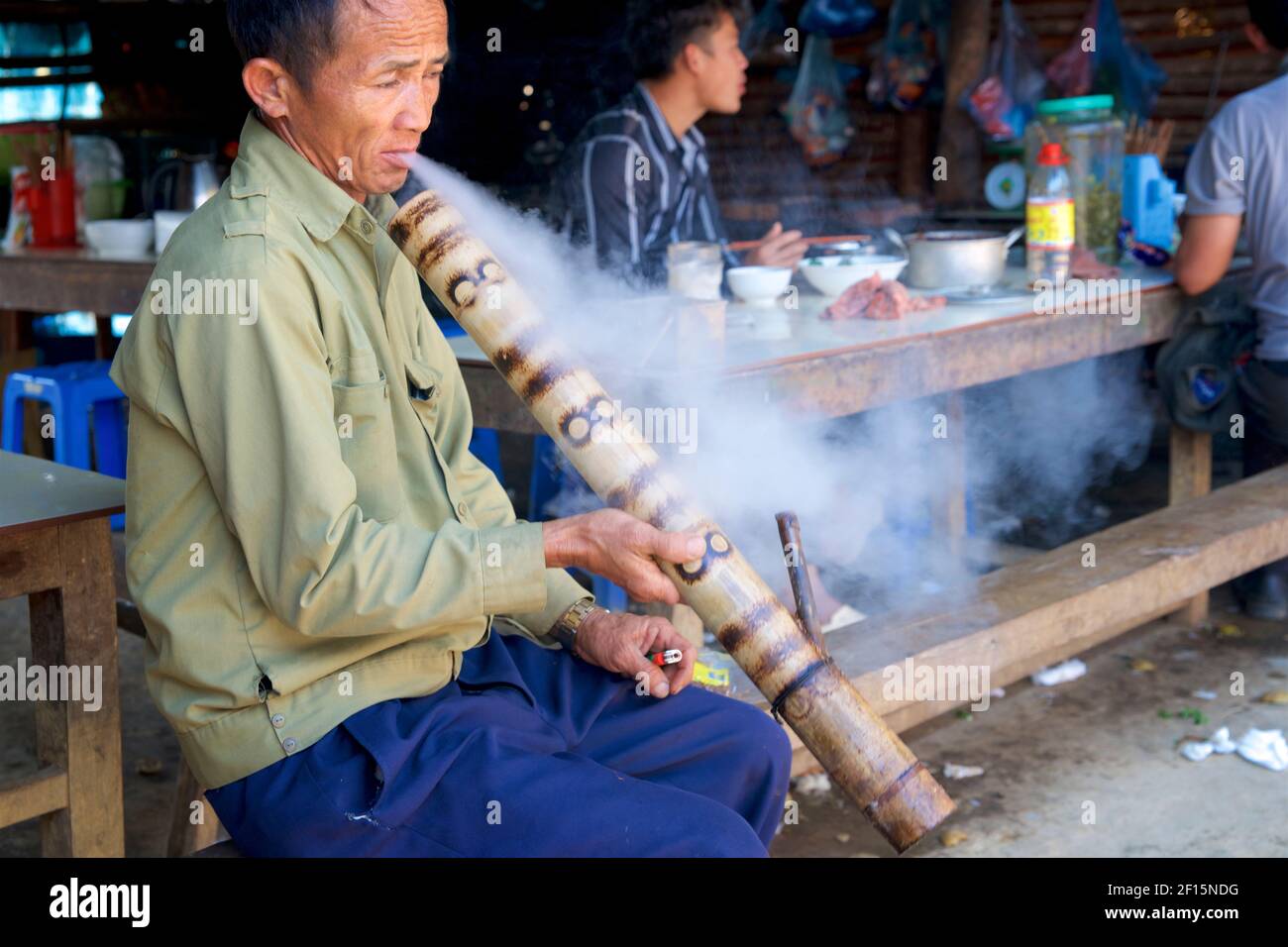 Vietnamese man at Can Cau market smoking from a bamboo water bong. Stock Photo