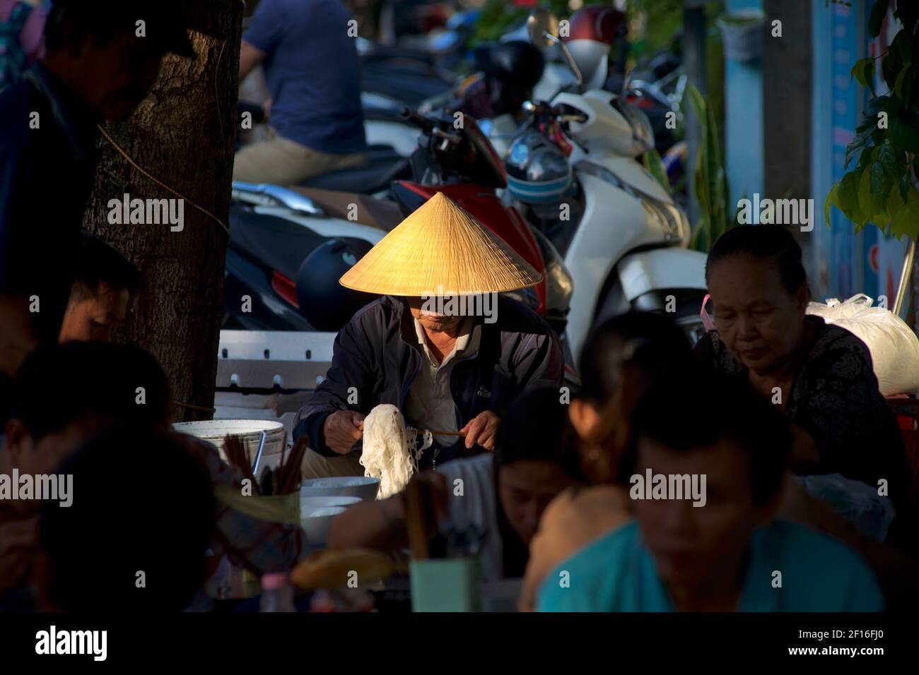 Vietnamese man in distinctive Vietnamese conical hat eating noodles at a roadside eatery, Hanoi, Vietnam. Stock Photo