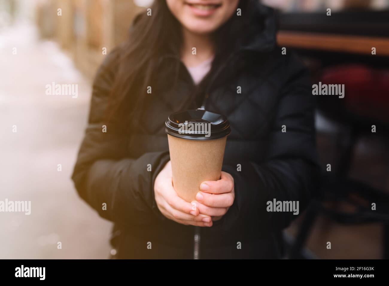 Smiling girl holds a paper cup of coffee in hand near cafe. High quality photo Stock Photo