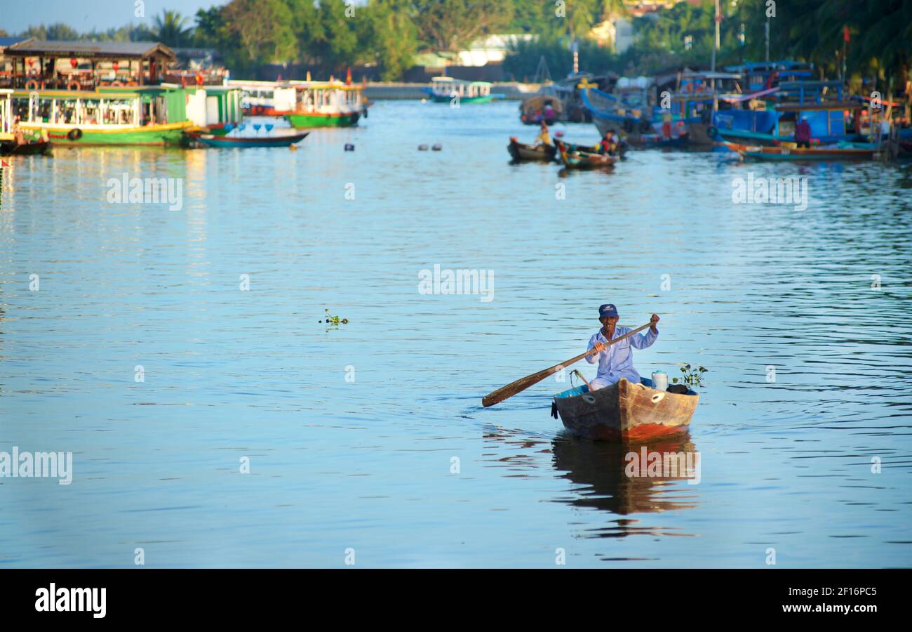 Vietnamese man rowing in a wooden boat on a canal off the Thu Bon river ...