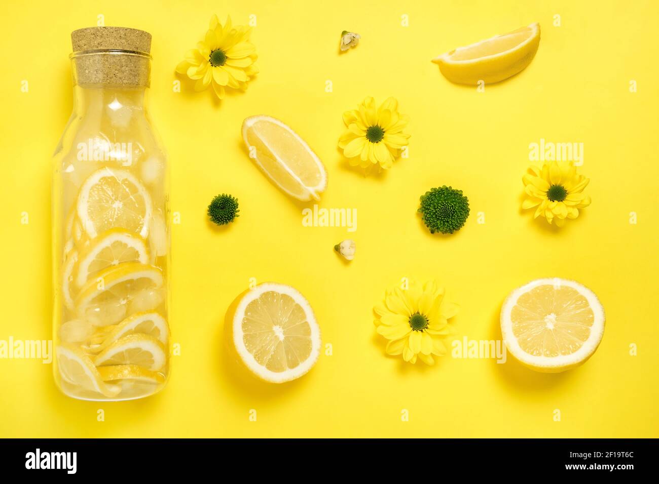 Flat lay Lemonade in glass bottle with lemons, flowers yellow paper background Stock Photo