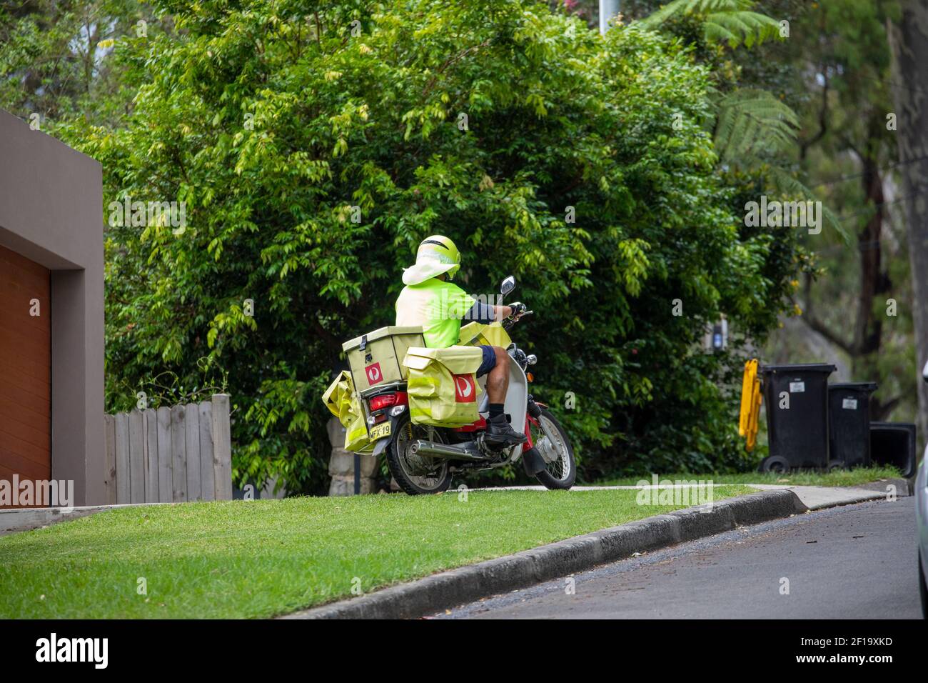 Australia postman riding motorbike delivers mail and letters to a Sydney home in Avalon,NSW,Australia Stock Photo