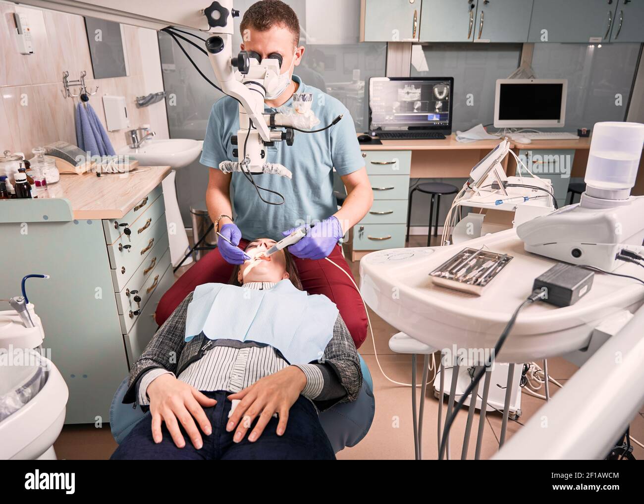 Young male dentist using microscope and dental instruments while