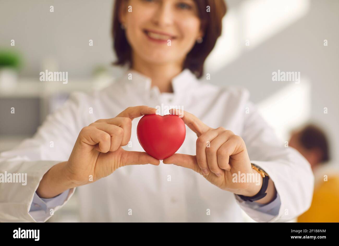 Heart symbol in hand of smiling female doctor cardiologist with stethoscope Stock Photo
