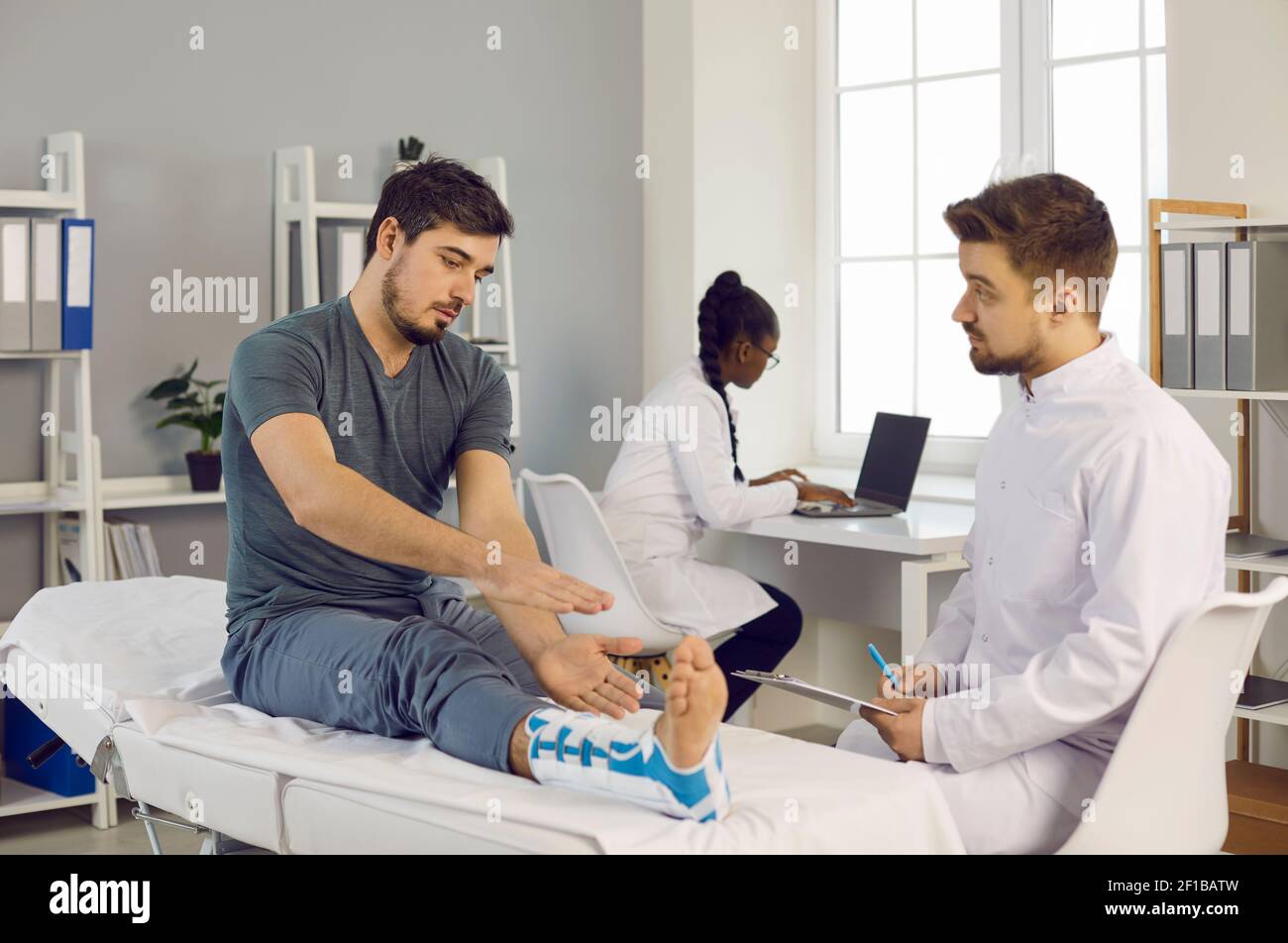 Man doctor listening complaints of male patient with injured broken leg Stock Photo