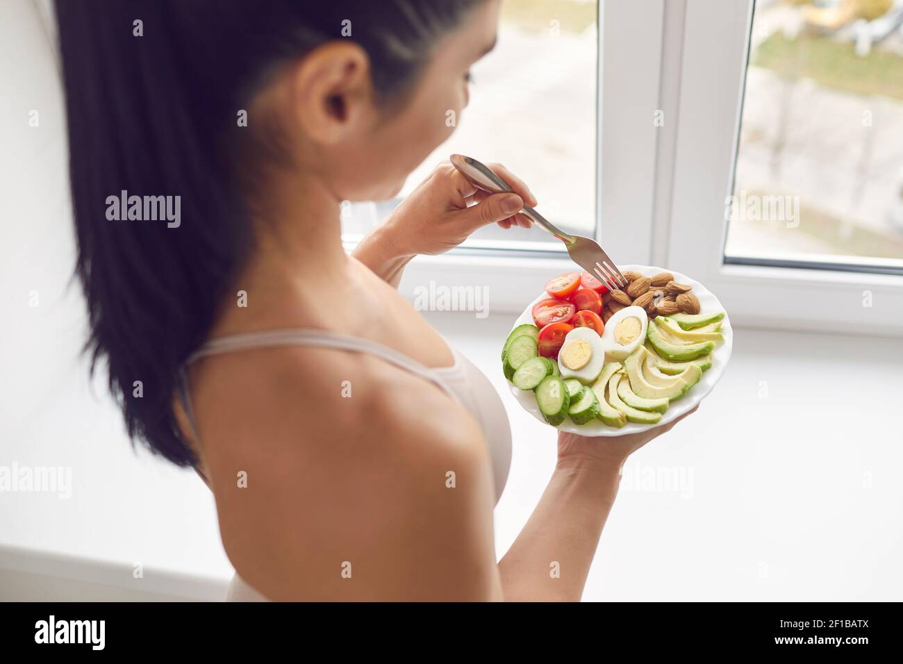 Young brunette fitness woman athete in sportswear standing and eating healthy meal Stock Photo