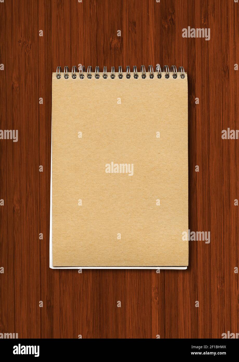 Spiral closed notebook mockup, brown paper cover, isolated on dark wood