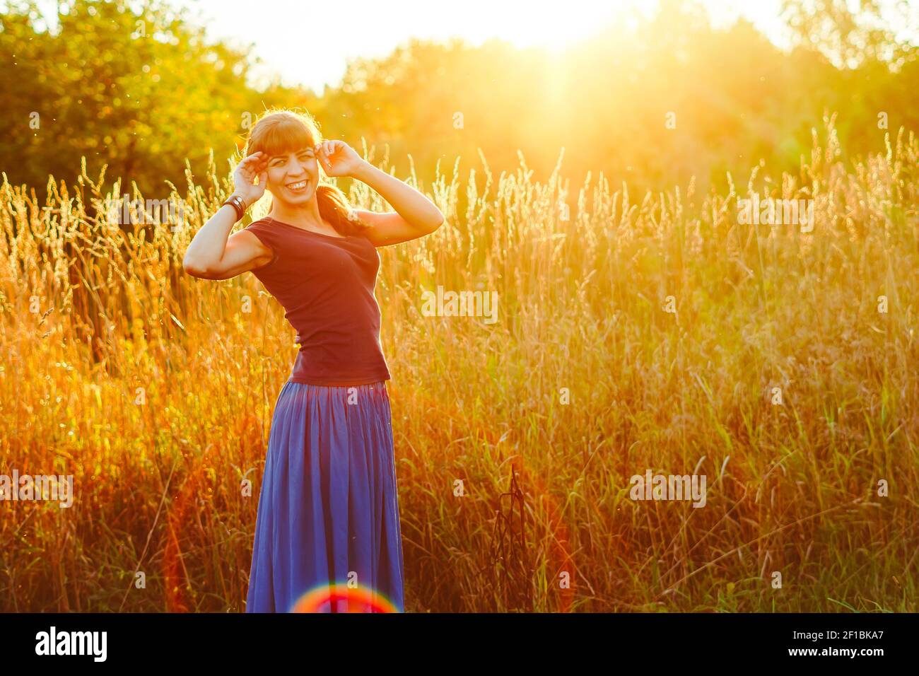 Young woman standing on a wheat field with sunrise on the background ...