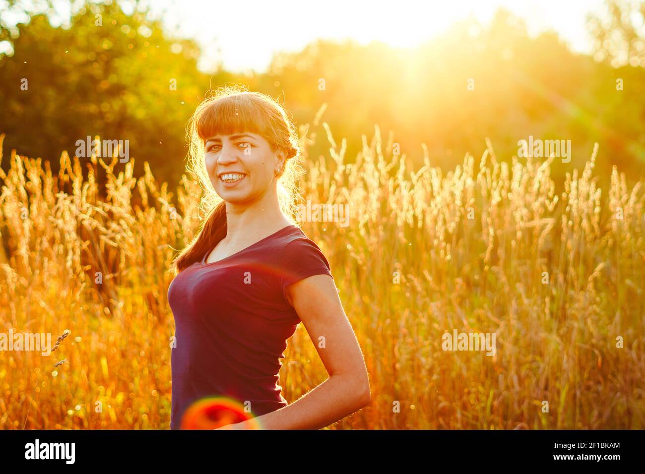 Young woman standing on a wheat field with sunrise on the background ...
