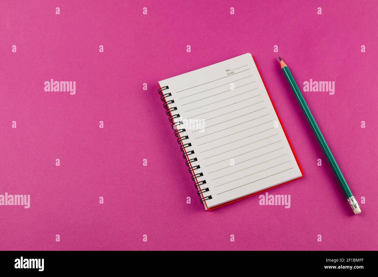 Open spring-loaded notebook and pencil on a pink background. White ...