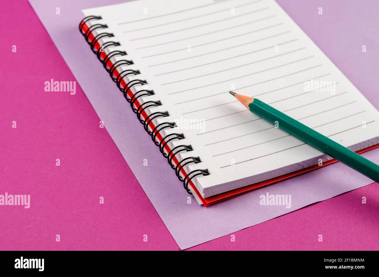 Open spring-loaded notebook and pencil on a pink background. White ...