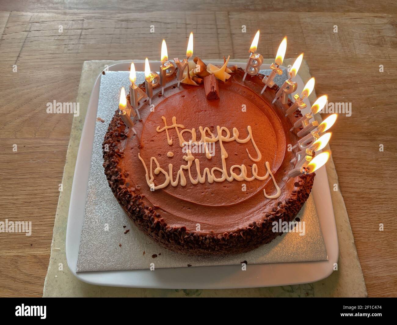 Home Made Chocolate Birthday Cake with Burning Candles on a Reclaimed Oak Kitchen Table Stock