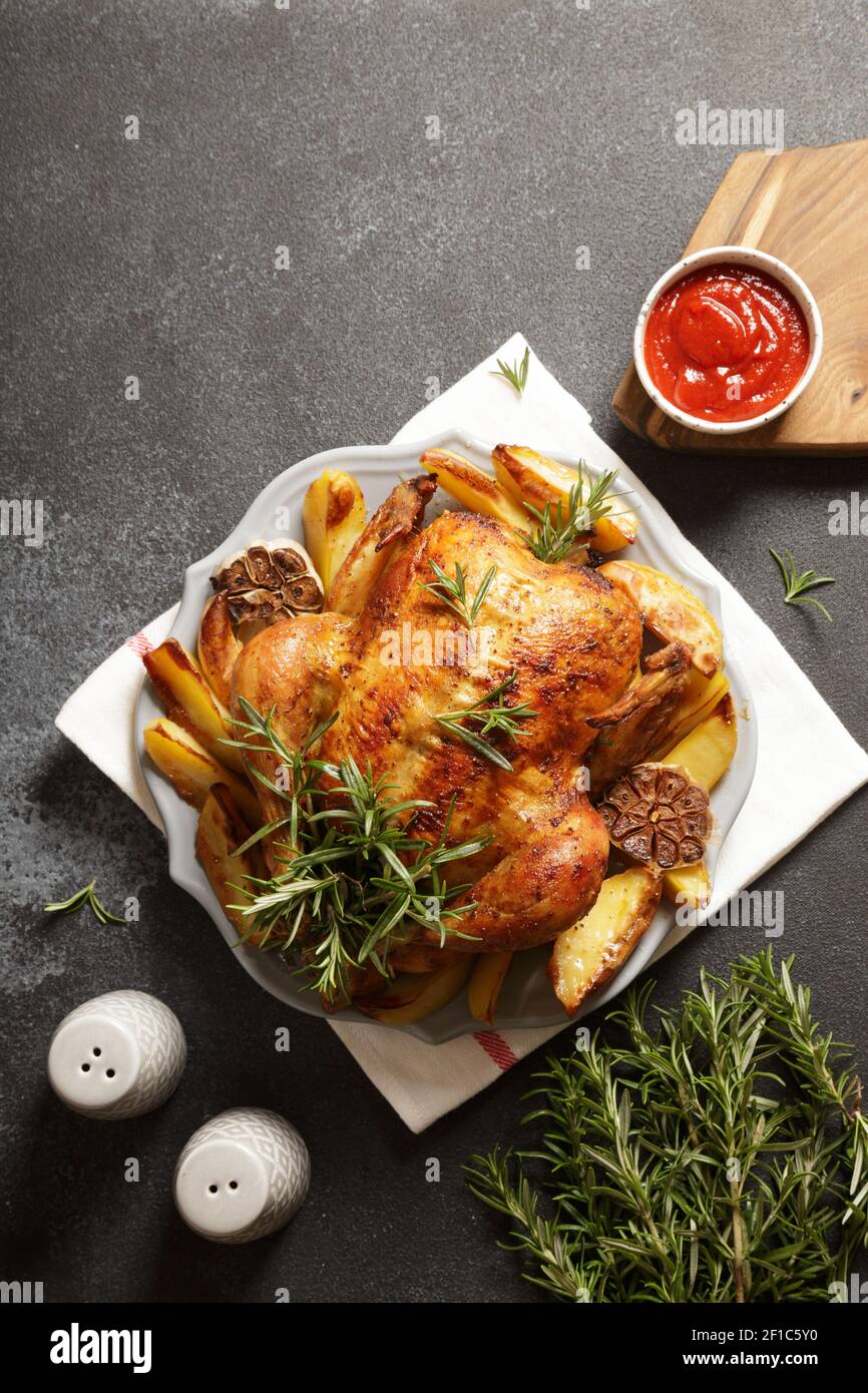 baked whole chicken with rosemary, garlic and ketchup on dack gray concrete background. roasted chicken Stock Photo